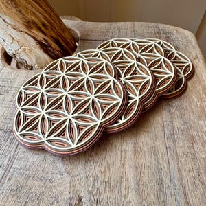 May include: Set of four wooden coasters featuring a layered flower of life design in shades of brown and white.