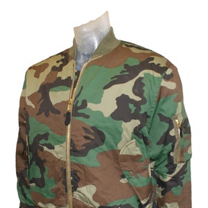 Peut inclure: Une veste bomber camouflage avec une fermeture éclair dorée et deux poches. La veste a un col et des poignets côtelés.