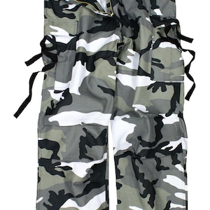 May include: Camouflage cargo pants in a gray, white, and black pattern. The pants have multiple pockets, a zipper fly, and black tie details. The pants are laid flat against a white background.