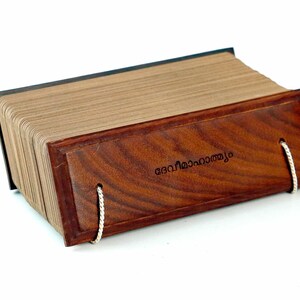 Puede incluir: Un libro encuadernado en cuero marrón con una cubierta de madera y un cierre de cuerda blanca. El libro está cerrado y la cubierta tiene el texto "കേരളത്തിലെ" en escritura malayalam.