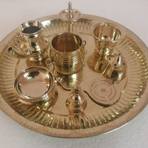 Op de afbeelding: Een messing puja thali met verschillende items, waaronder een diya, een kleine kom, een bel en een kleine wierookbrander.