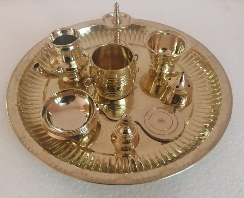 Op de afbeelding: Een messing puja thali met verschillende items, waaronder een diya, een kleine kom, een bel en een kleine wierookbrander.