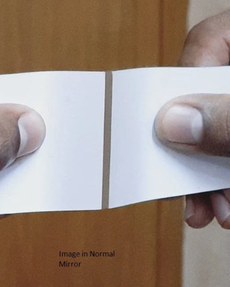 May include: A close-up of a white piece of paper folded in half. The paper is held by two hands, with the crease in the middle of the paper. The text "Image in Normal Mirror" is visible at the bottom of the image.
