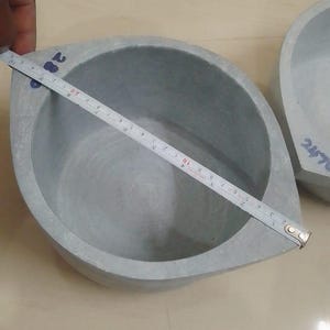 May include: A grey, leaf-shaped stone bowl with a rounded interior. A measuring tape shows the bowl is approximately 20 cm wide. The bowl is made of a solid, smooth material. Another bowl is partially visible in the background.