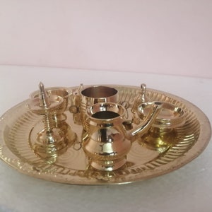 Op de afbeelding: Een set miniatuur puja-artikelen van messing op een decoratief dienblad. De set bevat een kleine pot, een kop, een bord en een diya.