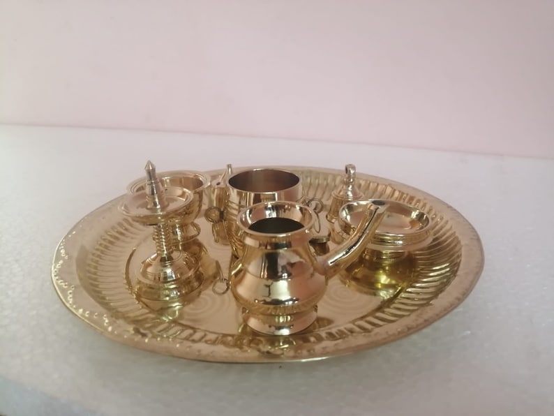 Op de afbeelding: Een set miniatuur puja-artikelen van messing op een decoratief dienblad. De set bevat een kleine pot, een kop, een bord en een diya.