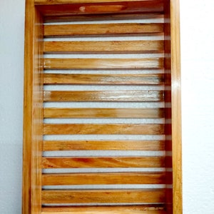 May include: Rectangular wooden tray with a slatted design. The tray is made of light brown wood and features a cutout handle on one side. The slats are evenly spaced, creating a visually appealing pattern. The tray is designed for serving or display.