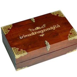 May include: A wooden box with gold accents and the inscription "śrīmad bhagavadgītā" on the top.