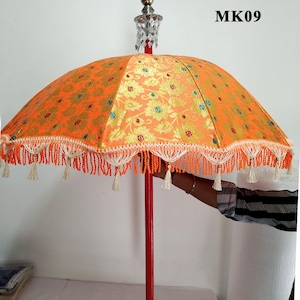 May include: Orange and gold fabric umbrella with white fringe trim and a red wooden handle. The umbrella has a crystal-like topper and the text "MK09" is visible in the top right corner of the image.