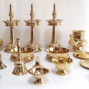 Op de afbeelding: Een verzameling religieuze messing voorwerpen, waaronder olielampen, kommen en kleine borden. De items zijn gerangschikt op een wit oppervlak. De lampen hebben een hoog, sierlijk ontwerp.