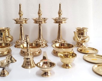 May include: A selection of brass religious items, including oil lamps, bowls, and small plates. The items are arranged on a white surface. The lamps have a tall, ornate design, and the bowls and plates are round.