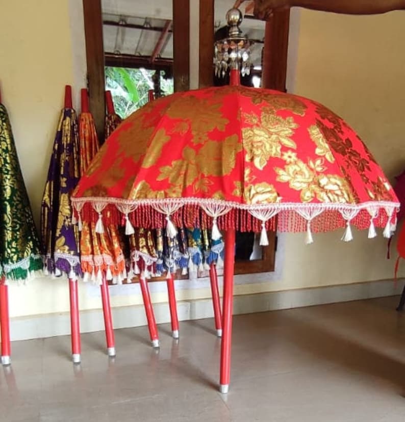 May include: A set of red and gold umbrellas with white fringe and tassels. The umbrellas are on red poles and are arranged in a row.