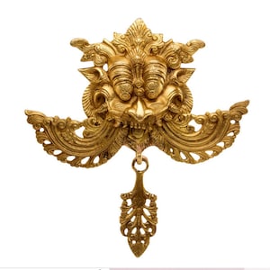 May include: A gold-coloured metal wall hanging featuring an intricate design of a mythical creature with a fierce expression. The hanging has elaborate details and a dangling ornament.
