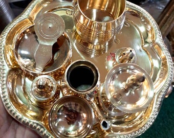 May include: A set of brass puja items, including a small plate, a cup, a spoon, a small pot, and a small incense burner. The items are arranged on a larger brass plate.