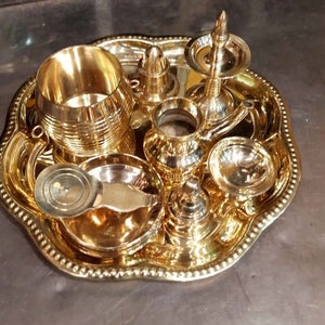 Op de afbeelding: Een set van gouden metalen ceremoni&euml;le voorwerpen op een decoratief dienblad. De set bevat een kleine kan, een kopje, een kom, een lepel en een kleine wierookbrander.