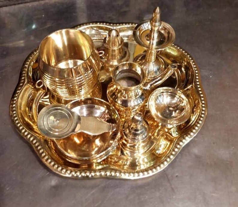 Op de afbeelding: Een set van gouden metalen ceremoni&euml;le voorwerpen op een decoratief dienblad. De set bevat een kleine kan, een kopje, een kom, een lepel en een kleine wierookbrander.