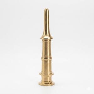 May include: A vertical brass fire hose nozzle featuring a tapered, slender top section that transitions into a wider, cylindrical body. The object has a series of horizontal ridges and a flat, circular base, showcasing a polished metallic finish.