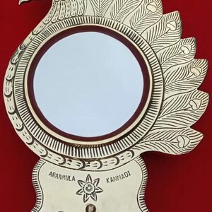May include: A gold-colored peacock-shaped mirror with a round, reflective surface. The mirror is decorated with intricate details and the words "Aranmula Kannadi" are inscribed on the base.