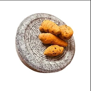 May include: A close-up of a grey stone mortar and pestle with four pieces of turmeric root on top.