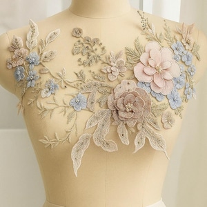 May include: Embroidered floral applique with pink, blue, and brown flowers, detailed leaves, and bead embellishments. The applique is displayed on a mannequin.
