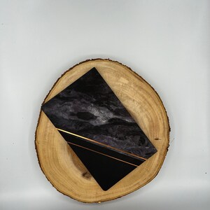 May include: A black and gold marble notebook on a wooden slice. The notebook has a black cover with gold lines and a marble pattern.