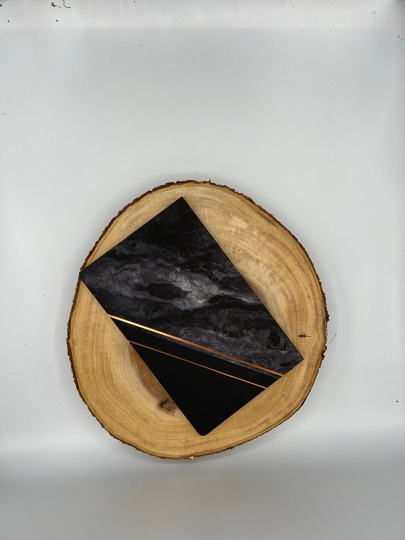 May include: A black and gold marble notebook on a wooden slice. The notebook has a black cover with gold lines and a marble pattern.