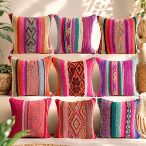 May include: A collection of nine square throw pillows arranged in three rows. Each pillow features a distinct woven texture with vibrant vertical stripes in shades of pink, orange, teal, purple, and red, accented by intricate geometric diamond patterns.