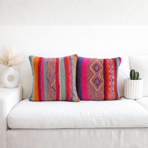 May include: Two square throw pillows featuring a vibrant, multi-colored woven pattern with vertical stripes, geometric diamond shapes, and a textured fabric finish. The colors include bright pink, orange, red, teal, and purple hues throughout.