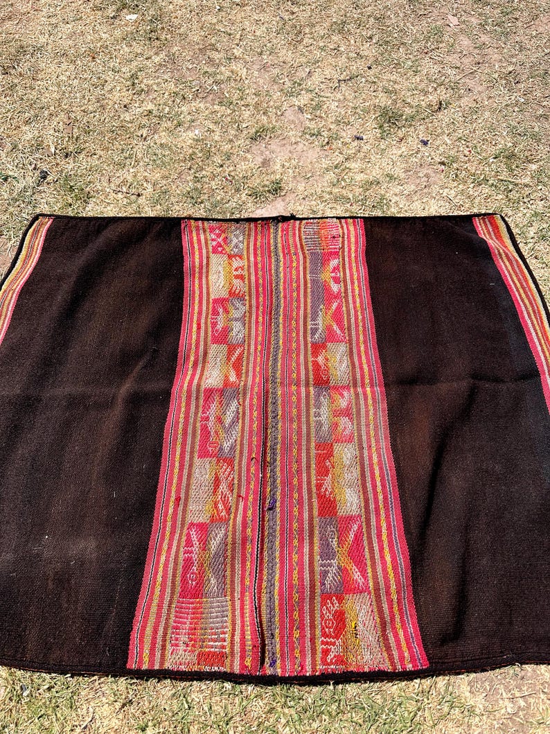 Op de afbeelding: Een zwarte alpaca wollen deken met een kleurrijke geweven rand. De rand heeft geometrische patronen in rood, geel en blauw.