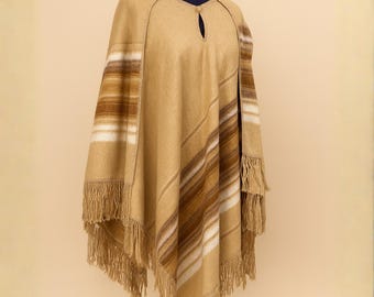 May include: A tan poncho with brown and white stripes and fringe. The poncho has a keyhole neckline and is displayed on a mannequin. The garment is made of a soft, woven material, ideal for cooler weather.
