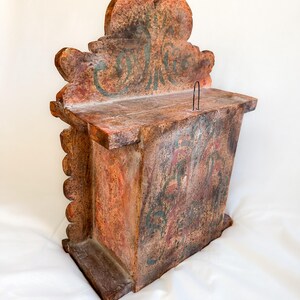 May include: A wooden box with a carved top and a painted inscription that reads "Collecte". The box is painted in shades of brown, red, and green.