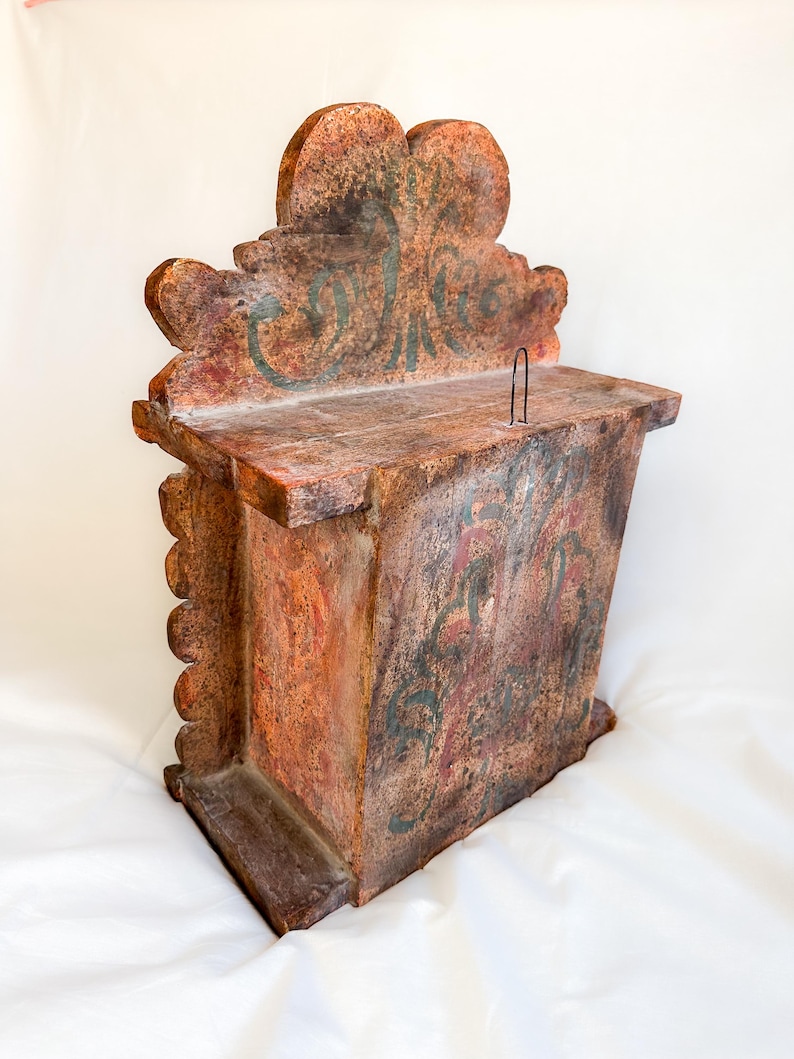 May include: A wooden box with a carved top and a painted inscription that reads "Collecte". The box is painted in shades of brown, red, and green.