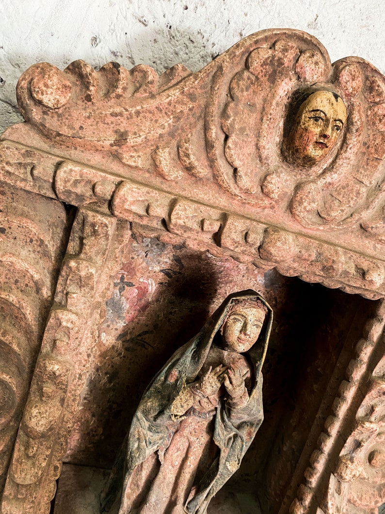 May include: A carved wooden niche with a painted figure of a woman in a robe. The niche has a decorative top with a carved face.