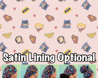 May include: A pink background with a repeating pattern of cartoon superheroes. The pattern includes Wonder Woman, Superman, Batman, and a female superhero. The text "Satin Lining Optional" is at the bottom of the image. Five different styles of surgical caps are shown below the text. The caps are printed with the same superhero pattern. The styles are labeled "Euro", "Ponytail", "Bouffant", "Tie Back", and "High Bun".