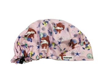 May include: Pink surgical scrub hat with a mermaid and seashell print. The hat has a drawstring and a label that says "PittsburghPE".