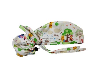 May include: A white scrub cap featuring a colorful Winnie the Pooh print with trees, bees, and the text "BUZZ BUZZ". The cap includes a black cord lock for adjustment, long fabric ties, and a small white tag labeled "PittsburghPE" on the side.
