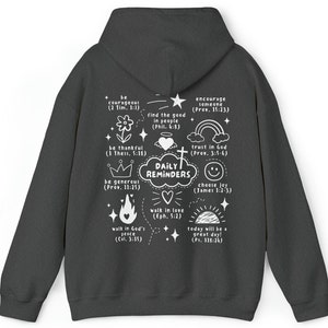 May include: A dark gray hoodie with a white print of daily reminders and bible verses. The print includes a cross, a heart, a crown, a rainbow, a star, a flame, a sun, and a smiley face.