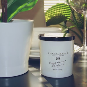 May include: White candle with a black lid and a label that reads "Luxe & Linger Luxe Candles Paris Views & Perfume Parfums d'Arome".