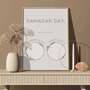 May include: A printable Ramadan Day sign with a light brown background and a white frame. The sign has the text "Ramadan Day" at the top and two circles with the text "Suhoor is at" and "Iftar is at" below. The circles are decorated with floral designs.