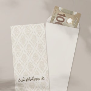 May include: A white envelope with a decorative pattern on the front. The envelope has a flap on the top and is open to reveal a Canadian $100 bill. The envelope has the text "Eid Mubarak" written on the front.