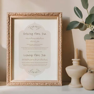 Puede incluir: Una impresión enmarcada con un fondo beige y un marco marrón. La impresión presenta dos oraciones islámicas, "Entering Home Dua" y "Leaving Home Dua", escritas en escritura árabe con traducciones al inglés debajo.