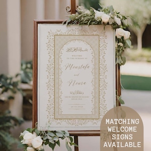 May include: A white wedding welcome sign with gold calligraphy and floral designs. The sign reads "Welcome to the Nikkah of Moustafa and Noura" and includes an Arabic quote and the date "30.12.2022".