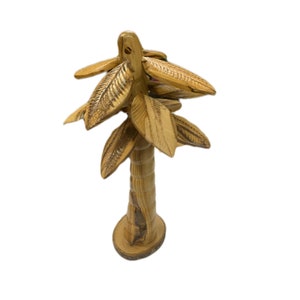 May include: A wooden palm tree sculpture with a brown, textured trunk and carved leaves. The tree is about 10 inches tall and is made of olive wood.