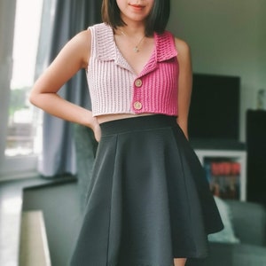 Könnte beinhalten: Ein rosa-beiges Häkel-Crop-Top mit Knopfverschluss. Das Top wird mit einem schwarzen Skaterrock kombiniert.