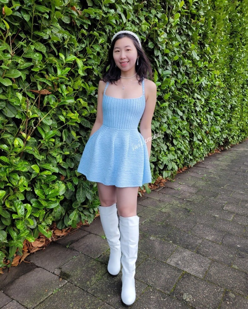 May include: A light blue crochet dress with a fitted bodice and a flared skirt. The dress is worn with white knee-high boots.