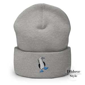 May include: A gray beanie featuring an embroidered blue-footed booby bird. The bird has black and white feathers with blue feet. The beanie is a soft knit material and has a folded cuff. The text "Dhlove Style" is on the lower right.