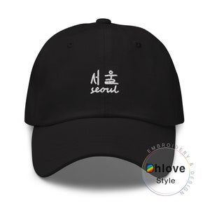 May include: Black baseball cap with white embroidered text in Korean characters and the English word "seoul". The cap has a curved brim and a top button. The embroidery is on the front of the cap.