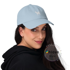 May include: Light blue baseball cap with a white embroidered dog design. The cap has a curved brim and an adjustable strap. The cap is made of a soft material and is suitable for everyday wear.