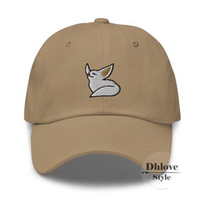 May include: A beige baseball cap with a curved peak. The cap has an embroidered design of a white and tan fox. The fox is in a relaxed pose with its eyes closed. The text "Dhlove Style" is printed on the lower right side of the cap.