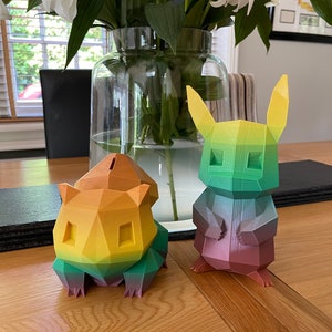 May include: Two colorful, 3D printed figurines of Pokemon characters. The figurine on the left is yellow, orange, and green, and the figurine on the right is green, purple, and pink.